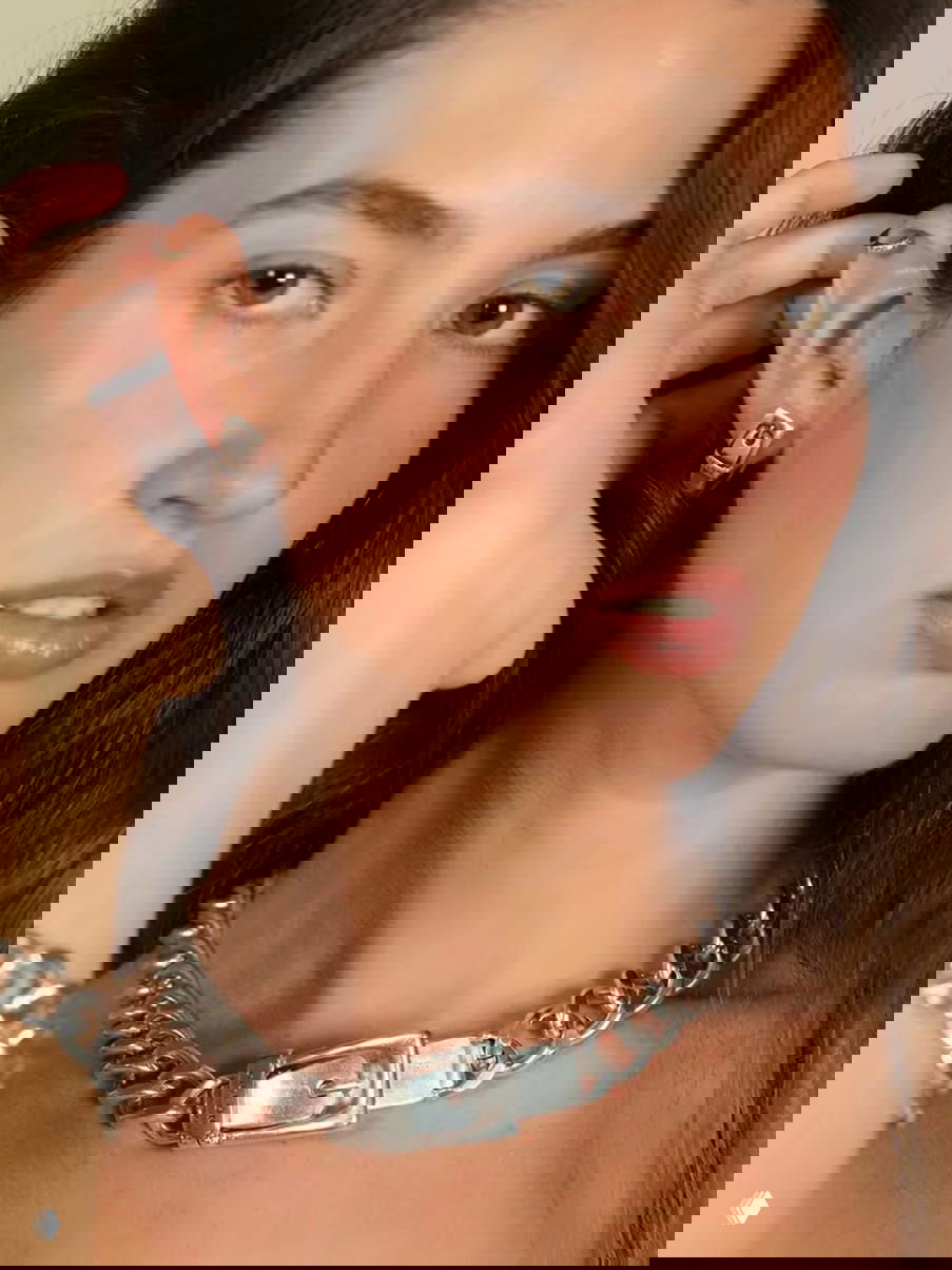 Рекламный кадр крупным планом: шея и плечо модели с массивным серебряным чокером-поясом и серьгами Ciclon, подчёркнуты естественным макияжем.