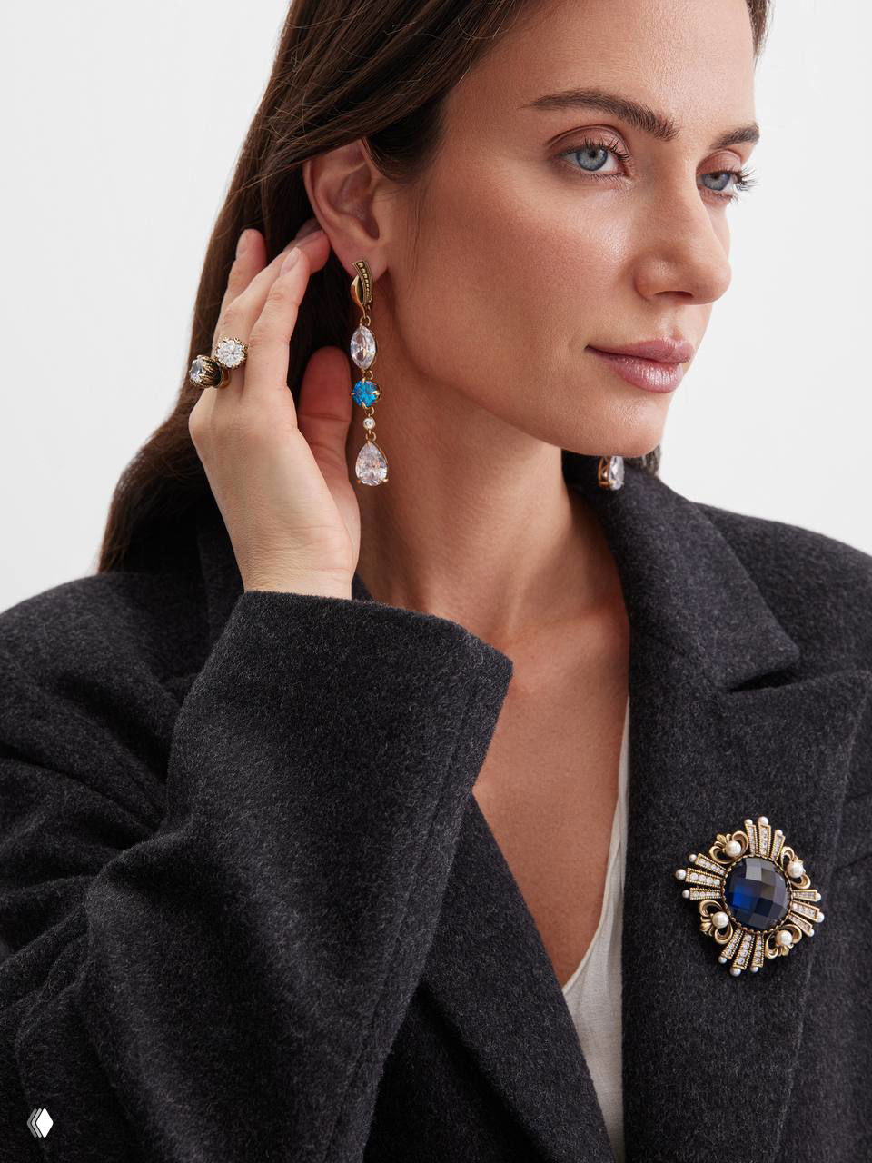 Крупный план модели в длинных подвесных серьгах и броши Fiore di Firenze на нейтральном фоне — сочетание кристаллов и золота.