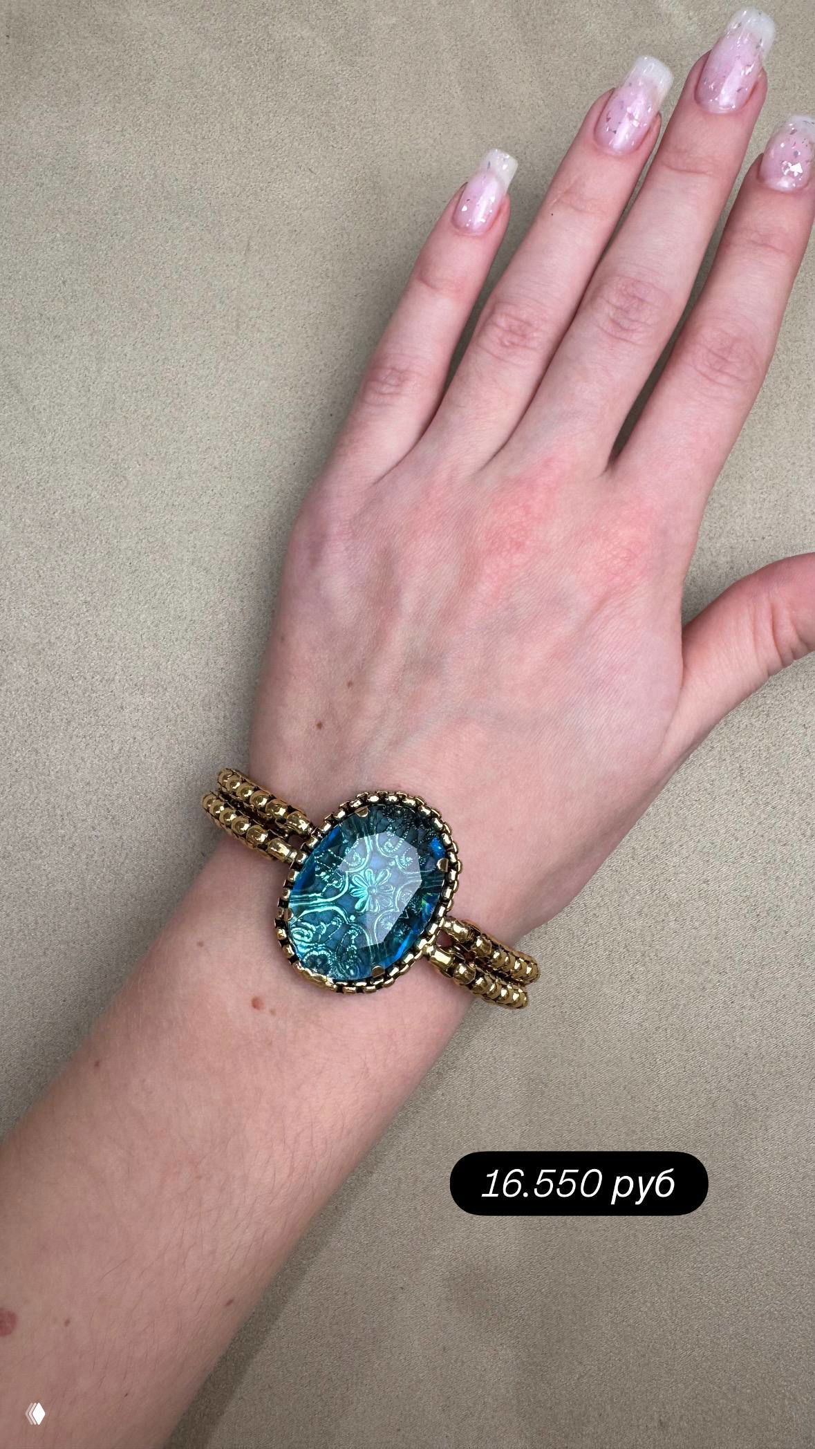 Запястье в браслете с голубым крупным кристаллом Filigrana на фоне бежевой подложки; видна детализация цветного стекла и металлической оправы.