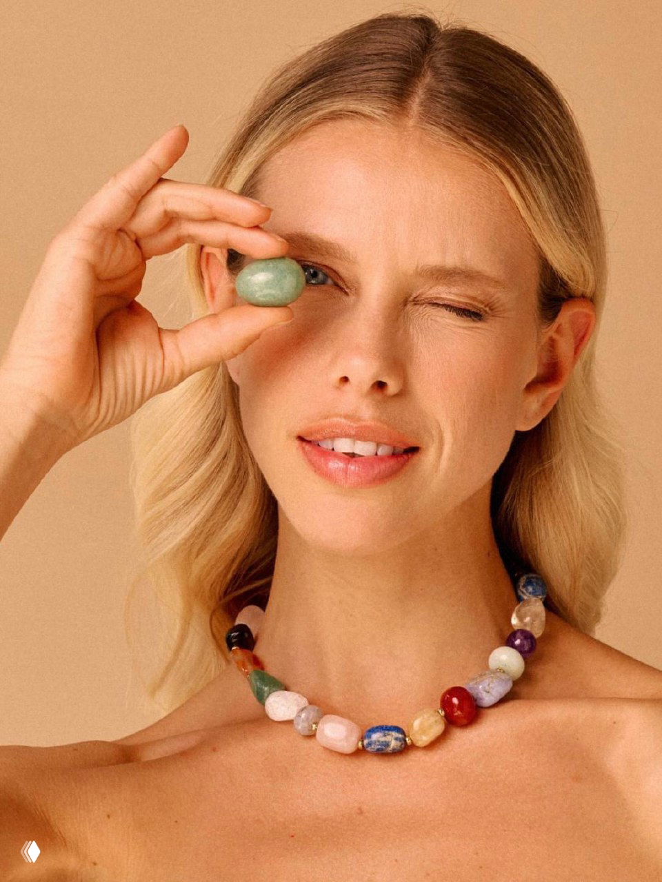 Портрет модели с ожерельем из разноцветных камней: натуральные бусины разных оттенков на шее, светлый нейтральный фон.