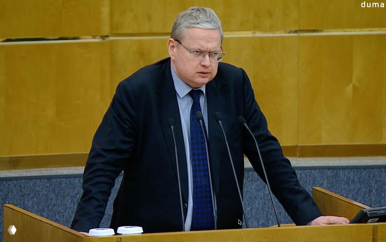 Депутат у трибуны в официальном зале заседаний Госдумы; микрофоны, деревянный пульт и строгий интерьер видны на фото.