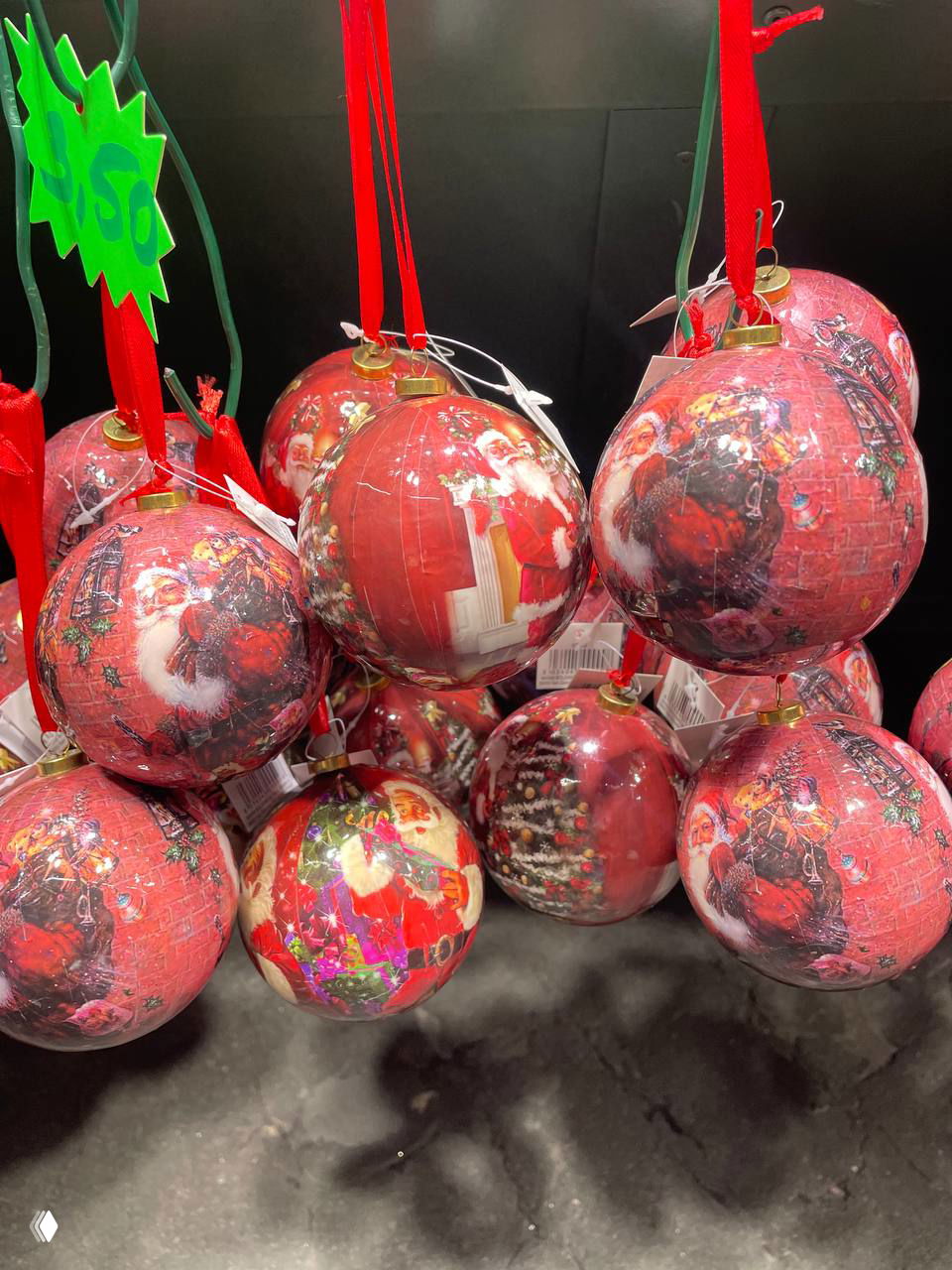 Красочные ёлочные шары красного цвета с изображениями и ленточками висят в торговом ряду рождественской ярмарки.
