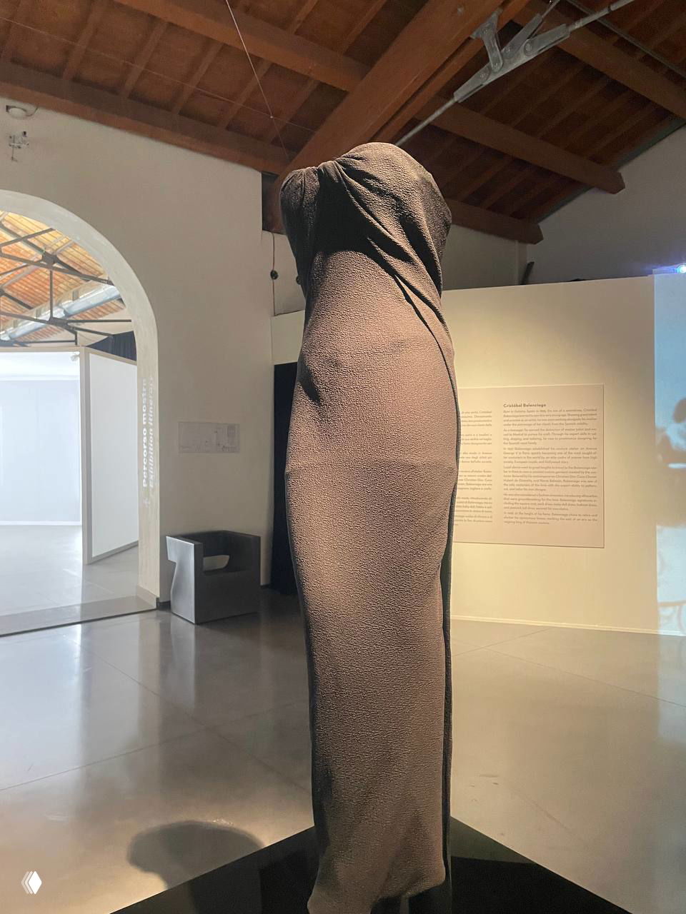 Крупный план одного из платьев: фактурная ткань, сжимающая силуэт, на фоне белых стен и арочной галереи маленького музея в Прато.