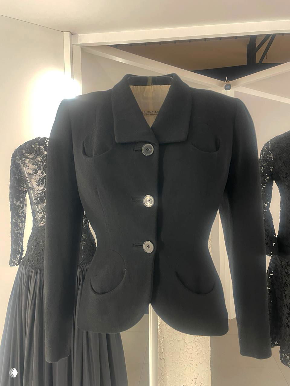 Манекен в длинном платье на фоне проекции архивных кадров: сочетание статичной одежды и движущегося изображения на белой стене.