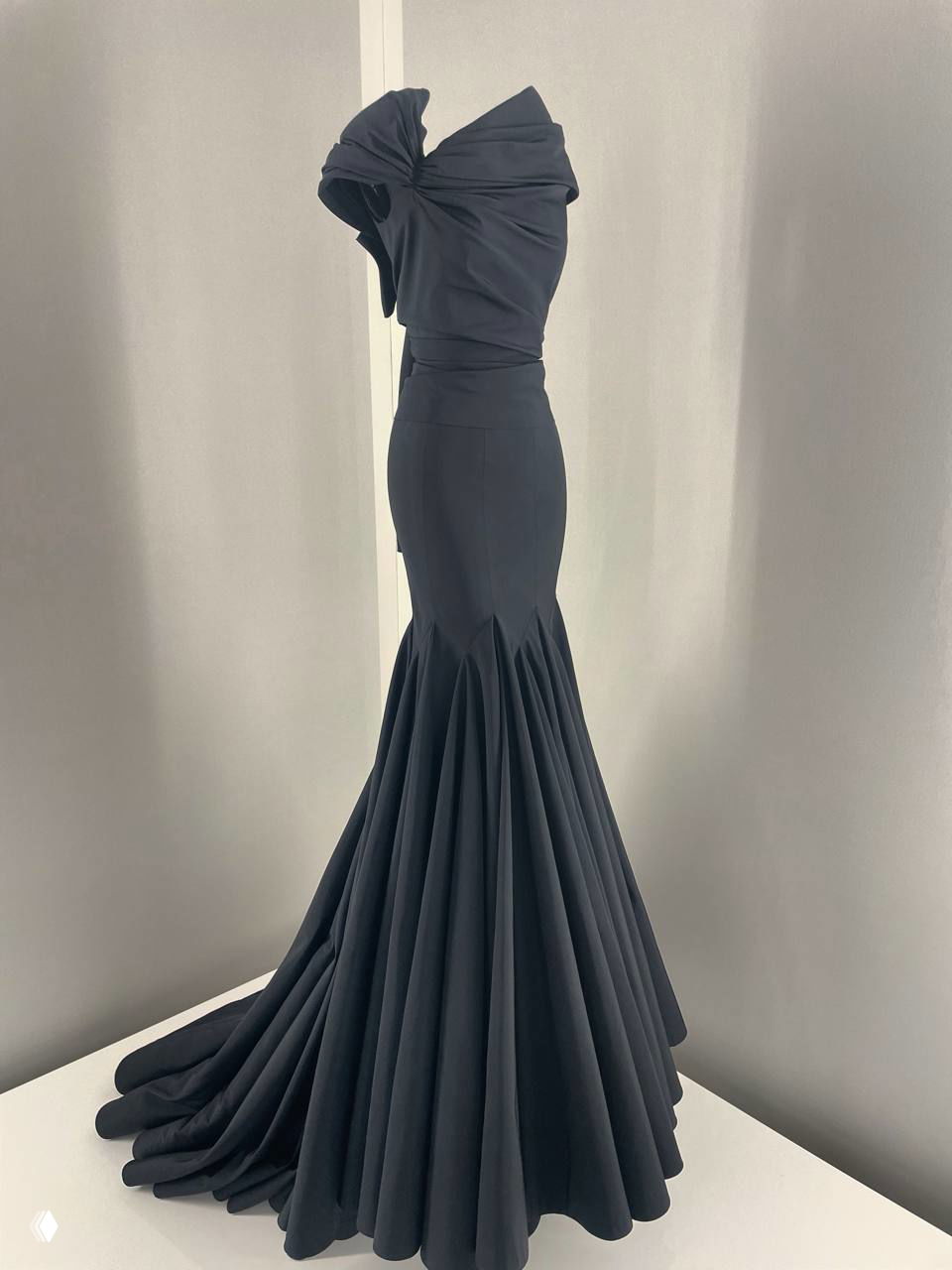 Черное вечернее платье с узким корсетом и длинным пышным шлейфом на подставке в минималистичной белой витрине — классический кутюрный образ.