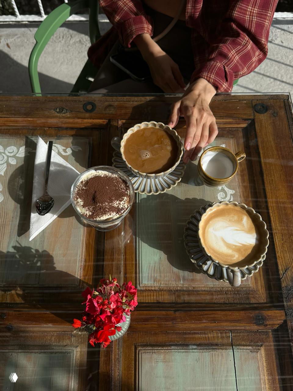Стеклянный стол с чашками кофе, десертом и рукой за чашкой — кадр из местного кафе, где отдыхают после трека на Ликийке.