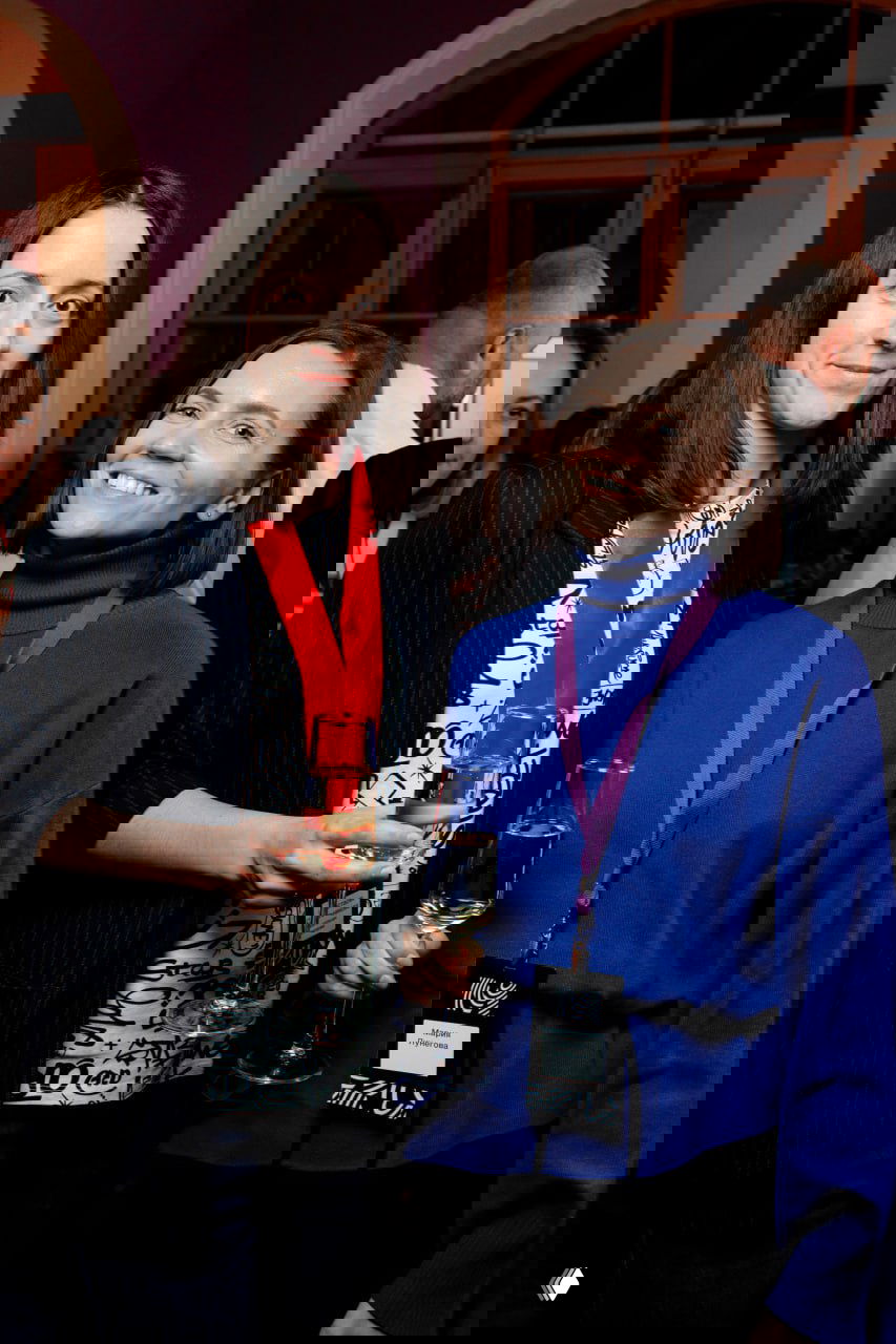 Неофициальное общение после встречи НАЭКК: две женщины с бокалами в руках, бейджи на шее, атмосфера нетворкинга и профессионального обмена