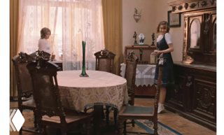 Ретро-интерьер столовой с круглым столом и сервировкой; две женщины у мебели, спокойная бытовая сцена в мягком освещении.