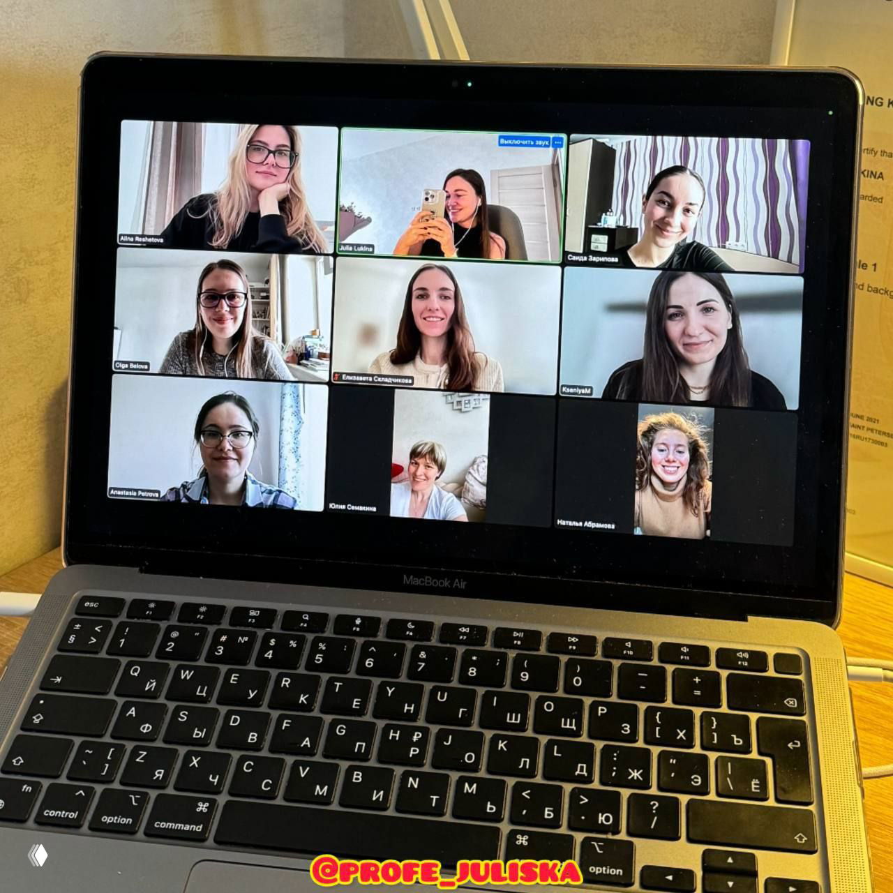 Экран ноутбука с видеоконференцией: несколько участниц разговорного клуба по испанскому в сетке Zoom на фоне клавиатуры MacBook и рабочего стола.