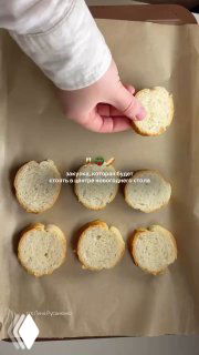 Рука укладывает запечённые кружочки багета на пергамент, подготовка закуски в форме новогоднего венка для праздничного стола