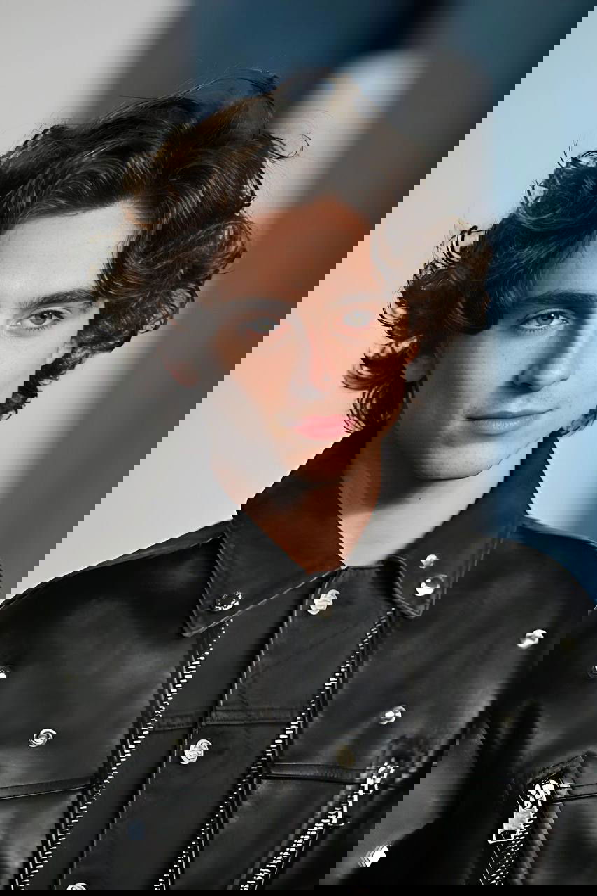 Портрет молодого мужчины с кудрявыми тёмными волосами в чёрной кожаной куртке, крупный план лица и плеч на нейтральном фоне