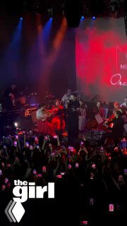 Фото с концерта Эмре Алтуга: сцена с музыкантами, актёр у микрофона на фоне красочного экрана, публика с телефонами.