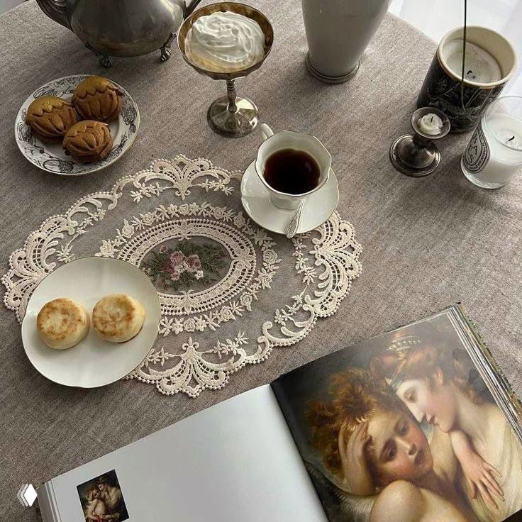 Сервировка чая на кружевной салфетке: чашка, печенье и книга в винтажном стиле — интерьерный кадр с романтической эстетикой.