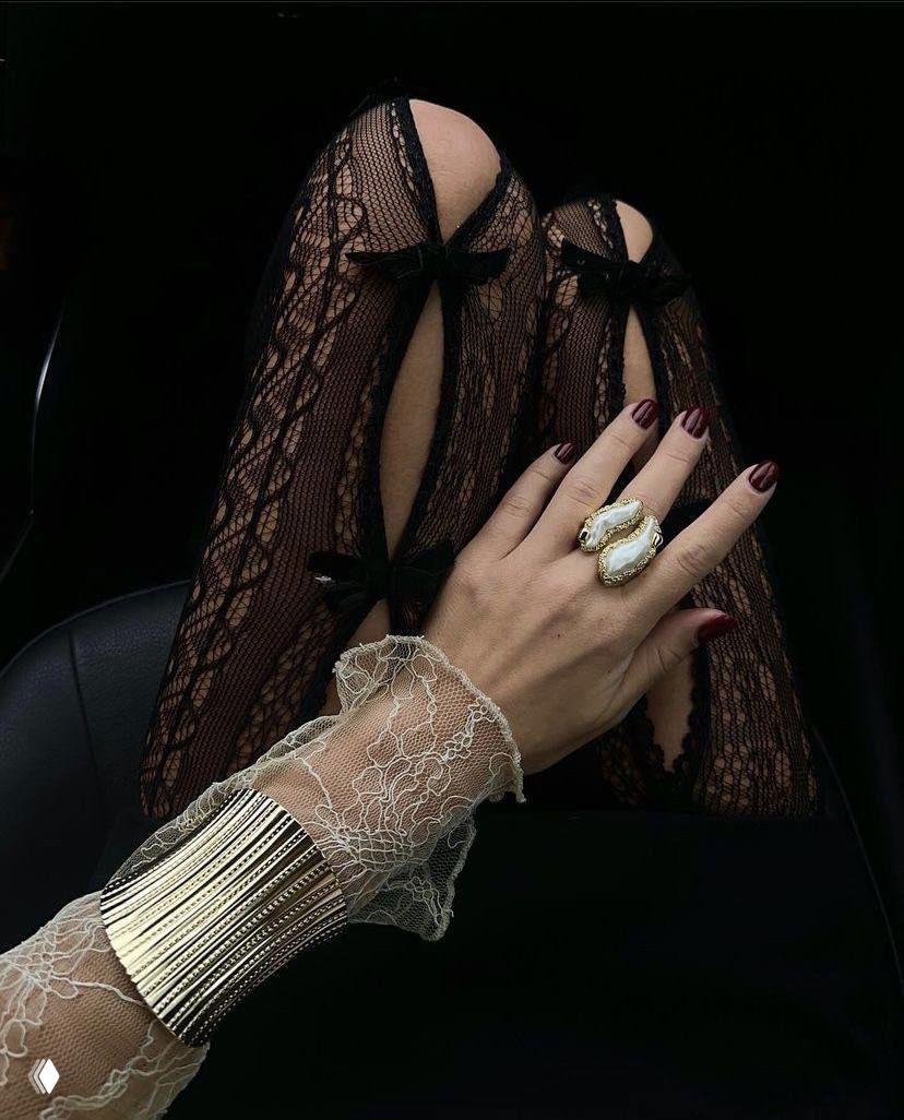 Рука в кружевной манжете, украшенная кольцом, на фоне чёрных кружевных чулок — акцент на винтажной детализации и гламурной эстетике.