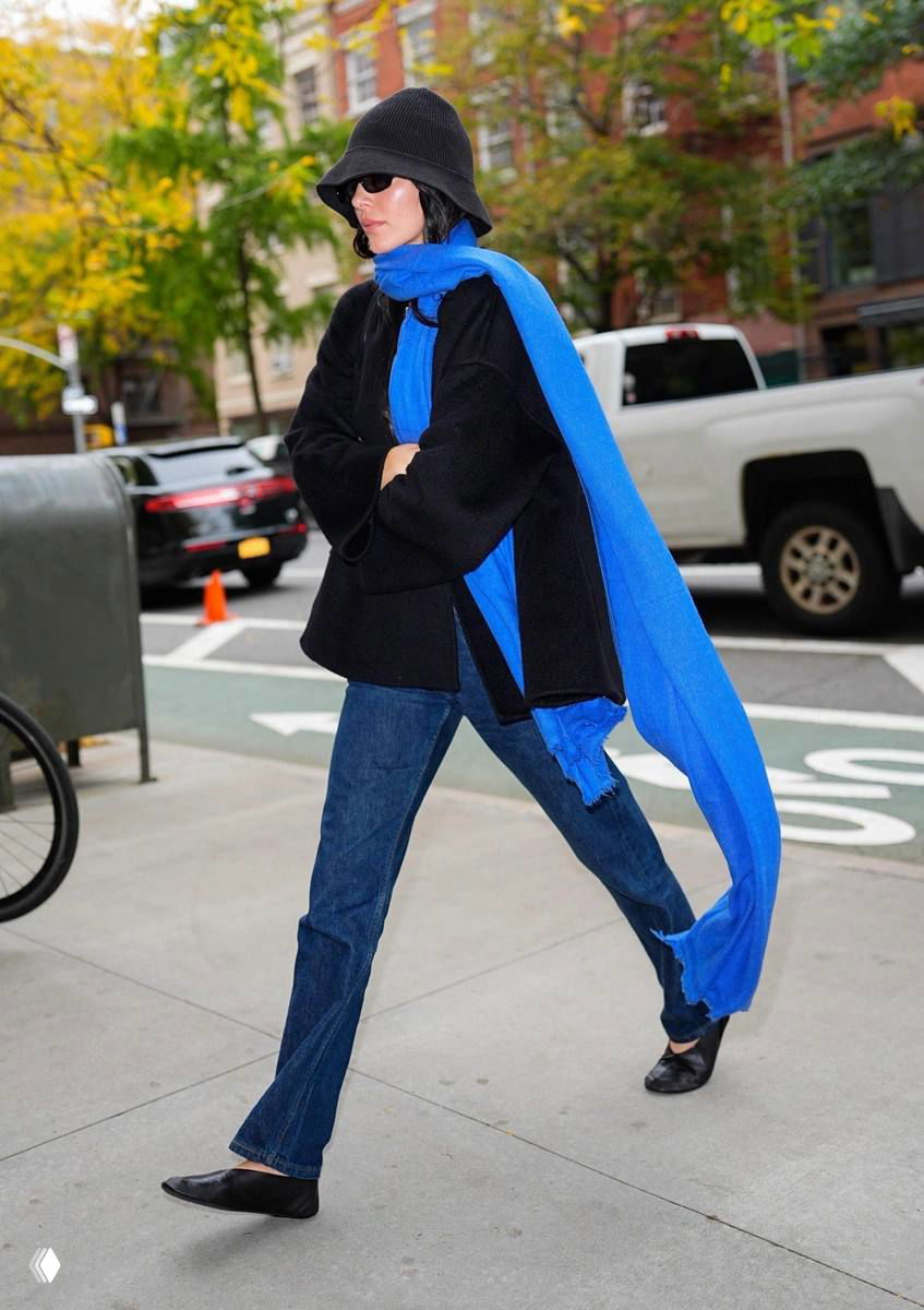 Кендалл Дженнер на улице в длинном насыщенно-синем шарфе, в черном верхнем слое и джинсах; уличный кадр с машинами и прохожими на заднем плане.
