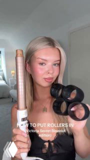 Девушка с платиновыми волосами держит стайлер и несколько бигуди в светлой комнате — подготовка к созданию объёмных локонов в стиле подиума.