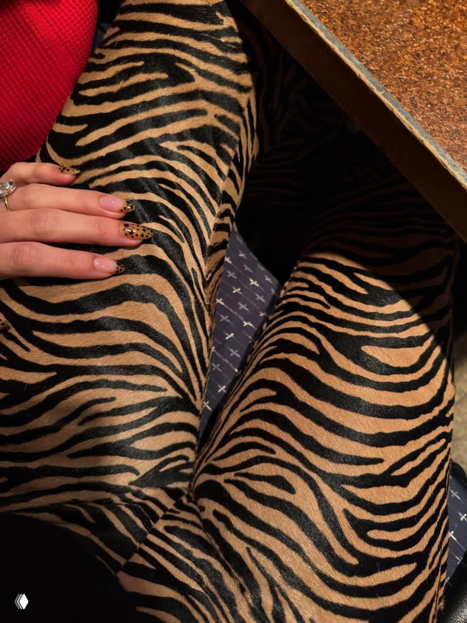 Ноги в анималистичных брюках с выразительным тёмно-бежевым рисунком, на руке видно леопардовый акцентный маникюр и несколько колец.