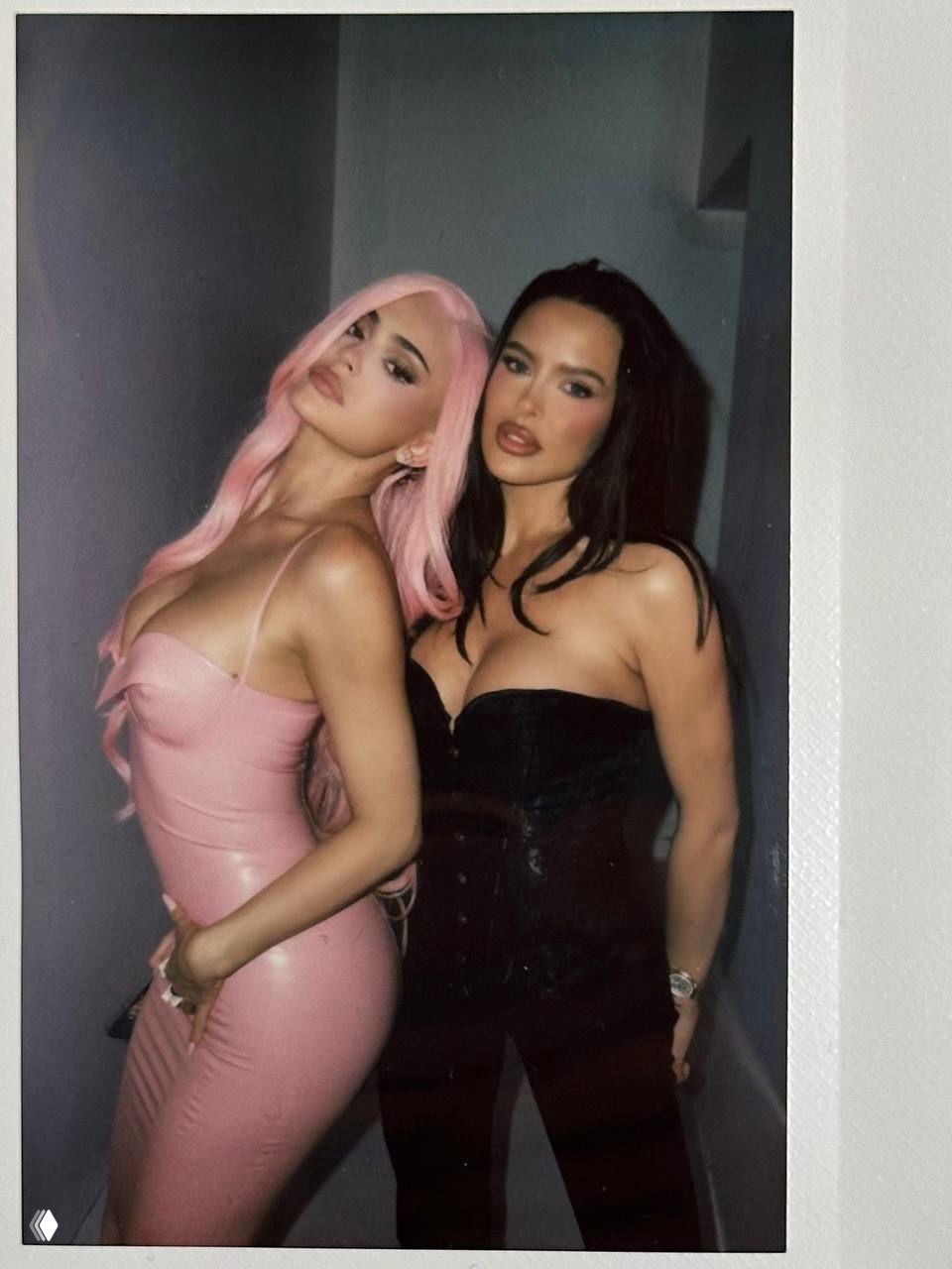 Две женщины в коридорной зоне вечеринки: слева фигура в облегающем светло-розовом латексном платье и длинных розовых волосах, правая в тёмном наряде.