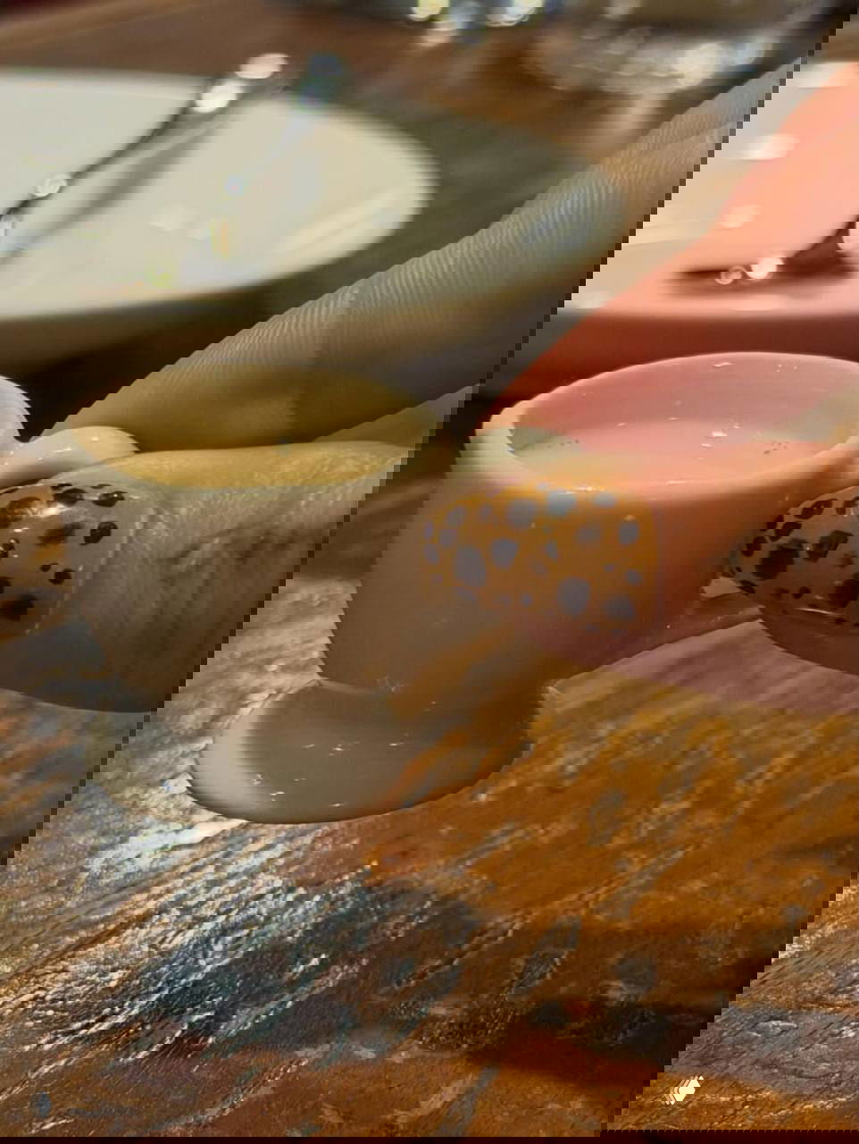 Крупный план пальца с необычным леопардовым маникюром: коричневая база и тёмные пятна на фоне деревянного стола и кофейной чашки.