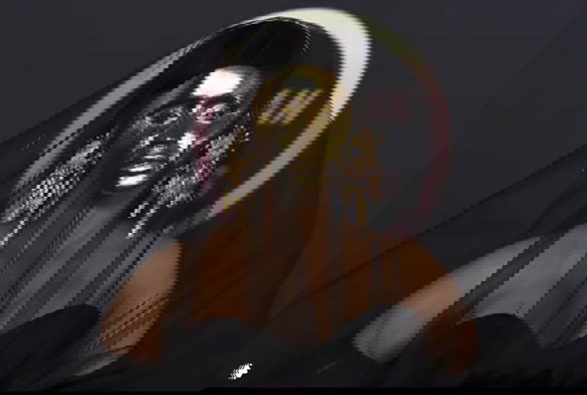 Крупный план человека на красной дорожке в золотой лицевой маске и чёрной вуали, видны массивные серьги и декоративные детали образа.