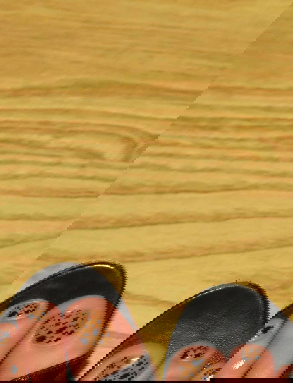 Педикюр в коричневых тонах с контрастными чёрными пятнами в леопардовом стиле на ногах в открытой обуви на деревянном полу.