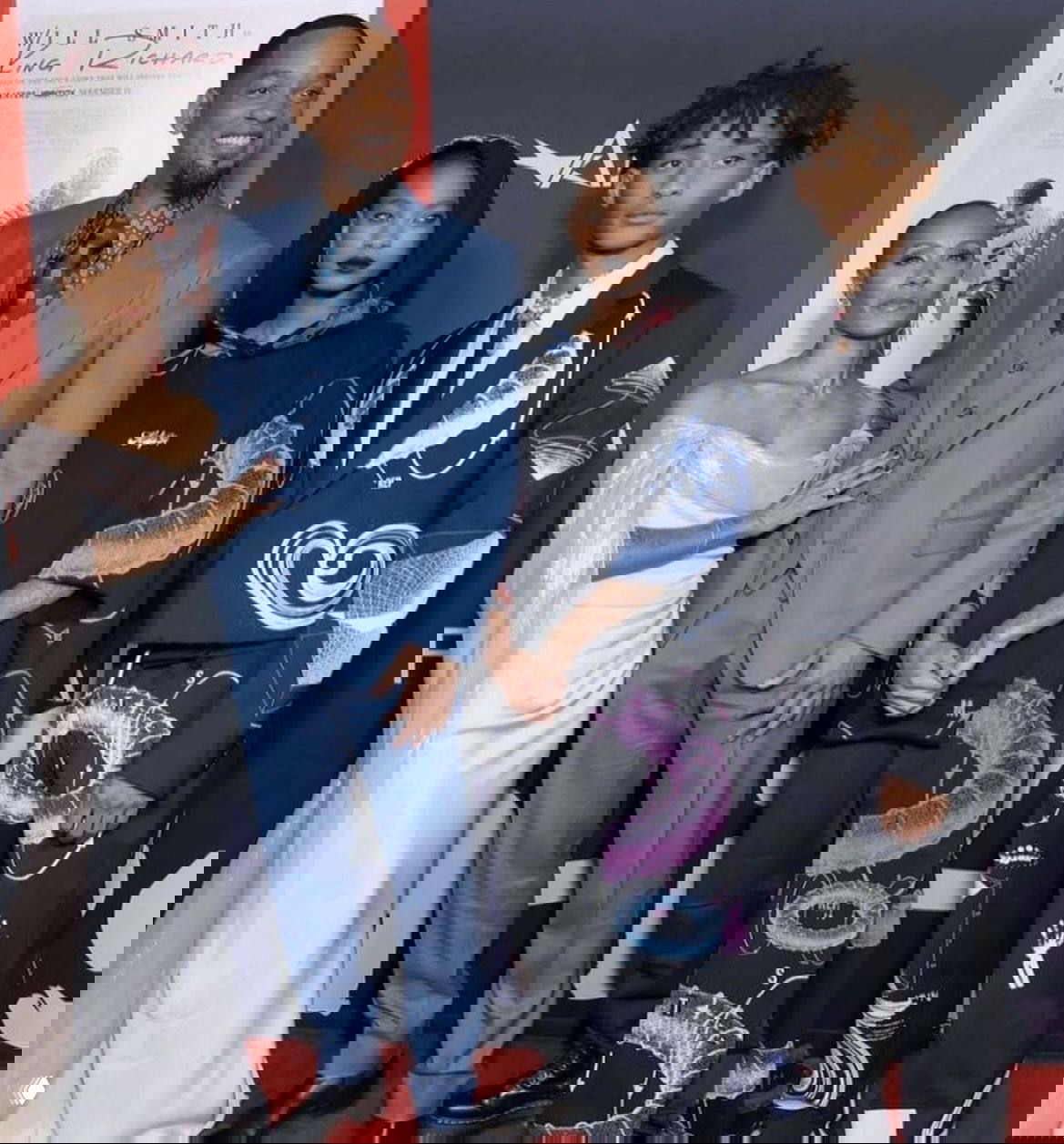 Групповая фотография на красной дорожке: несколько людей в эффектных нарядах на фоне киноафиши и фотокамер.