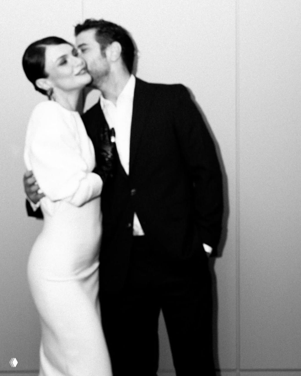 Черно‑белый фотокадр: Синем Унсал и Берк Джанката в интимном жесте — поцелуй и объятие на фоне нейтральной стены, атмосферный снимок.