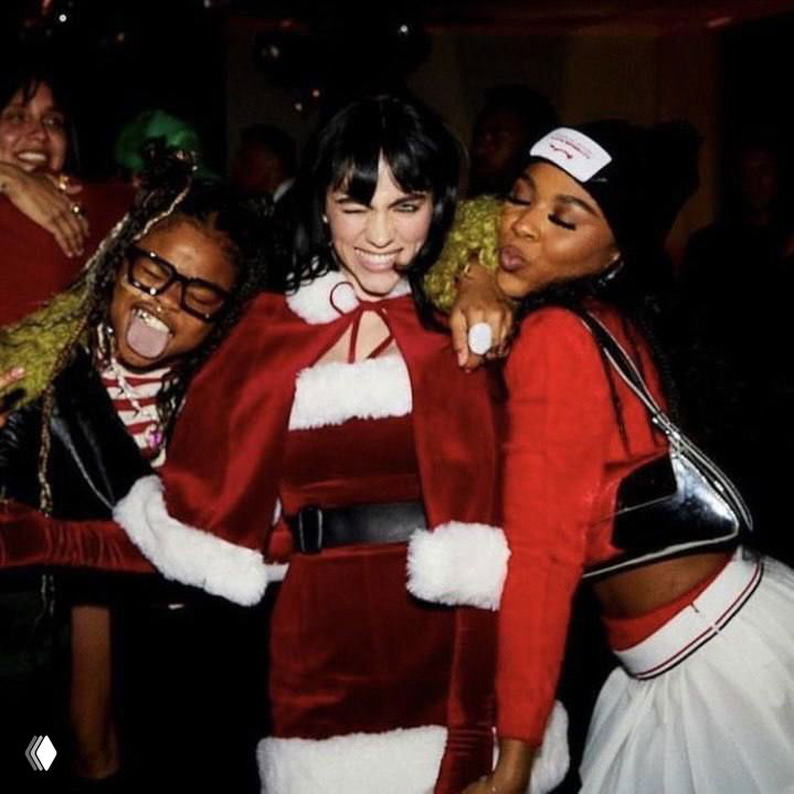 Групповое фото: Билли Айлиш в красном костюме Санты вместе с друзьями, улыбки и объятия на новогодней встрече.