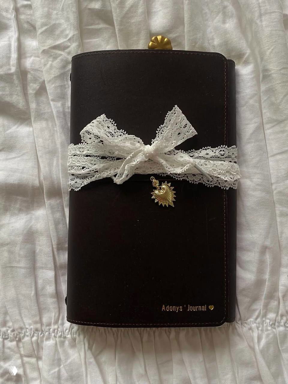 Чёрный кожаный блокнот с кружевной лентой и золотым кулоном на постели — аксессуар для ежедневника и записей в стиле poetcore.