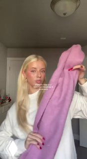 Крупный план: девушка с длинными светлыми волосами держит лиловый шарф в комнате — кадр из видеотуториала по способам завязывания шарфа, демонстрация приёма.