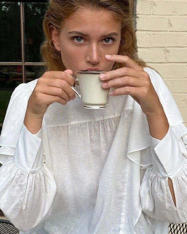 Портрет девушки в белой рубашке, которая держит чашку чая — натуральный снимок с акцентом на текстуру тканей и спокойную, меланхоличную атмосферу.