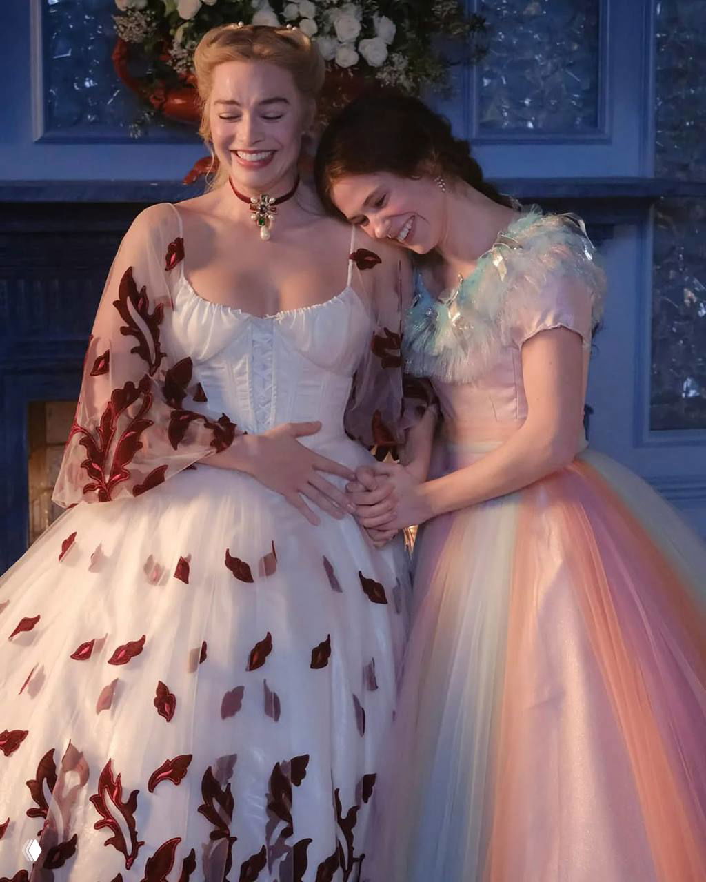 Две актрисы в пышных платьях на фоне камина; тёплая сцена с жестом дружбы и атмосферой костюмной драмы.