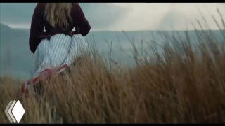 Кадр из трейлера фильма: фигура в платье идёт по высокому травяному полю на фоне туманного холма — атмосферный и романтичный образ.