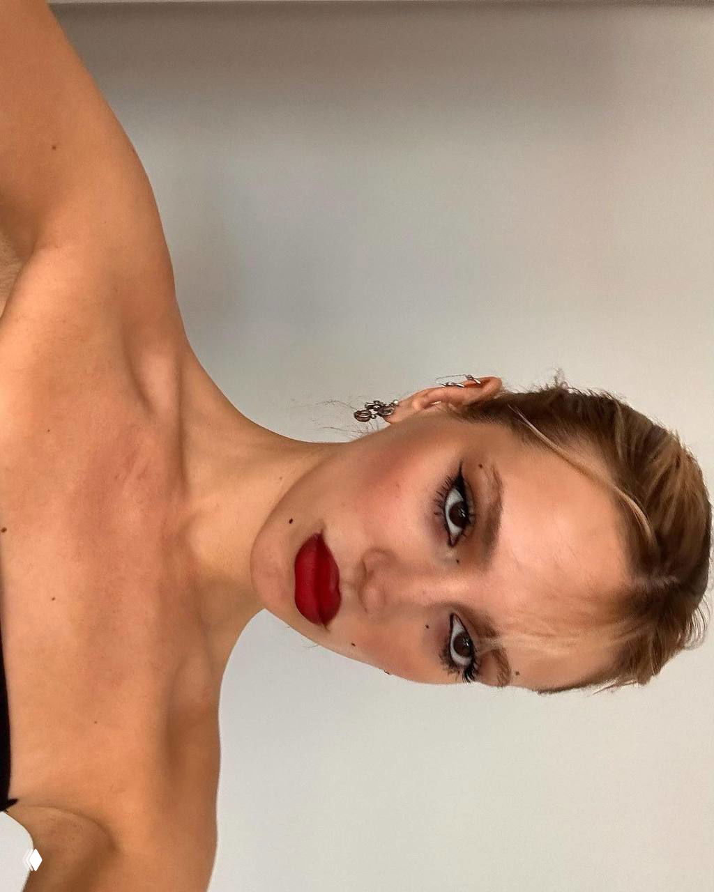 Ближайший план: светловолосая девушка с яркой алой помадой, аккуратный макияж глаз и светлый фон, акцент на губах.