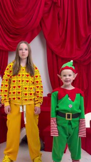 Портретная сцена с молодой певицей в жёлтом костюме и маленьким эльфом на фоне красных портьер — кадр из новогодней съёмки, подчёркивающей вирусность трека.