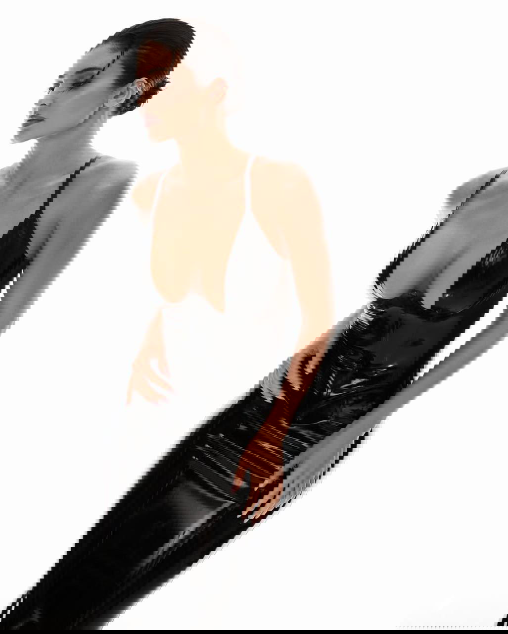 Модель в обтягивающем лаковом чёрном платье в полный рост на белом фоне, акцент на силуэте и корсетной посадке.