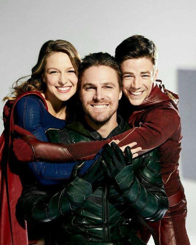 Три человека в костюмах супергероев в студийной фотосессии: красный, зелёный и синий элементы костюмов, все улыбаются.