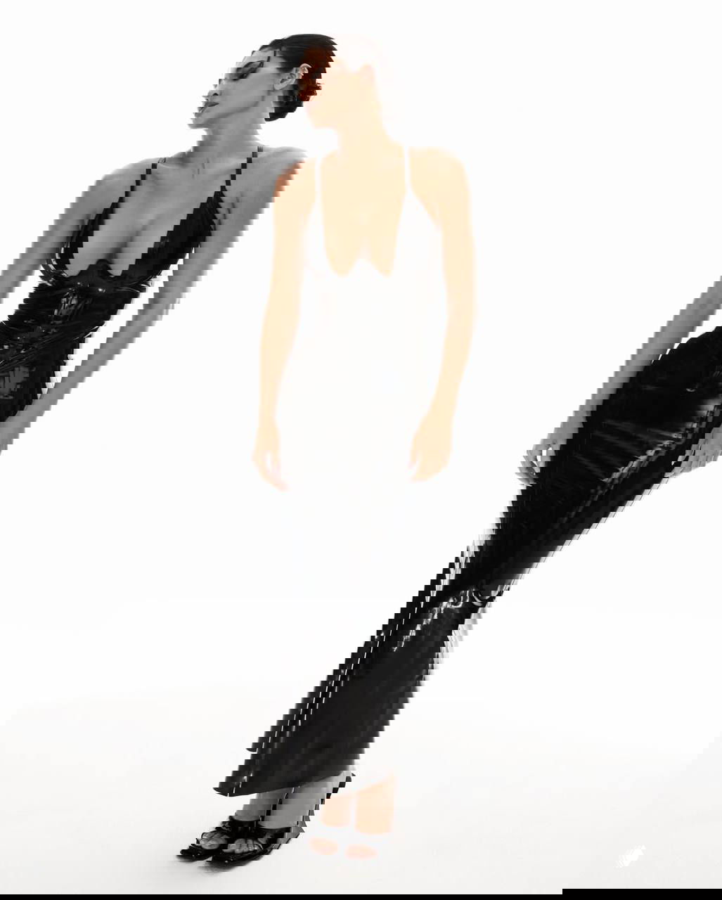 Фотография в полный рост: лаковое чёрное платье KHY подчёркивает талию и бедра модели, чистый белый фон студии.