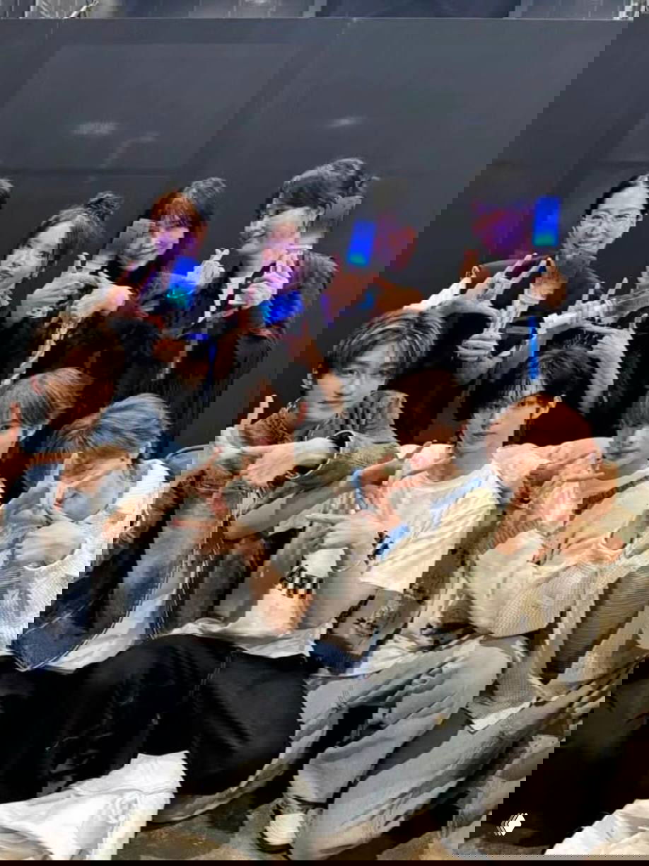 Групповая фотография: молодые айдолы и команда визажистов демонстрируют светящиеся рекламные аксессуары и позируют после совместной работы.