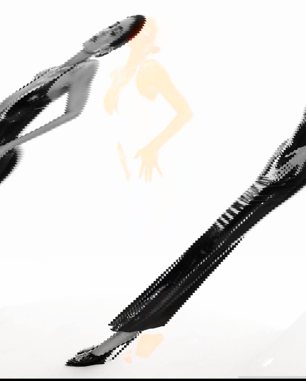 Профильный ракурс модели в глянцевом чёрном платье KHY: акцент на изгибах, корсетной талии и длинном подоле.