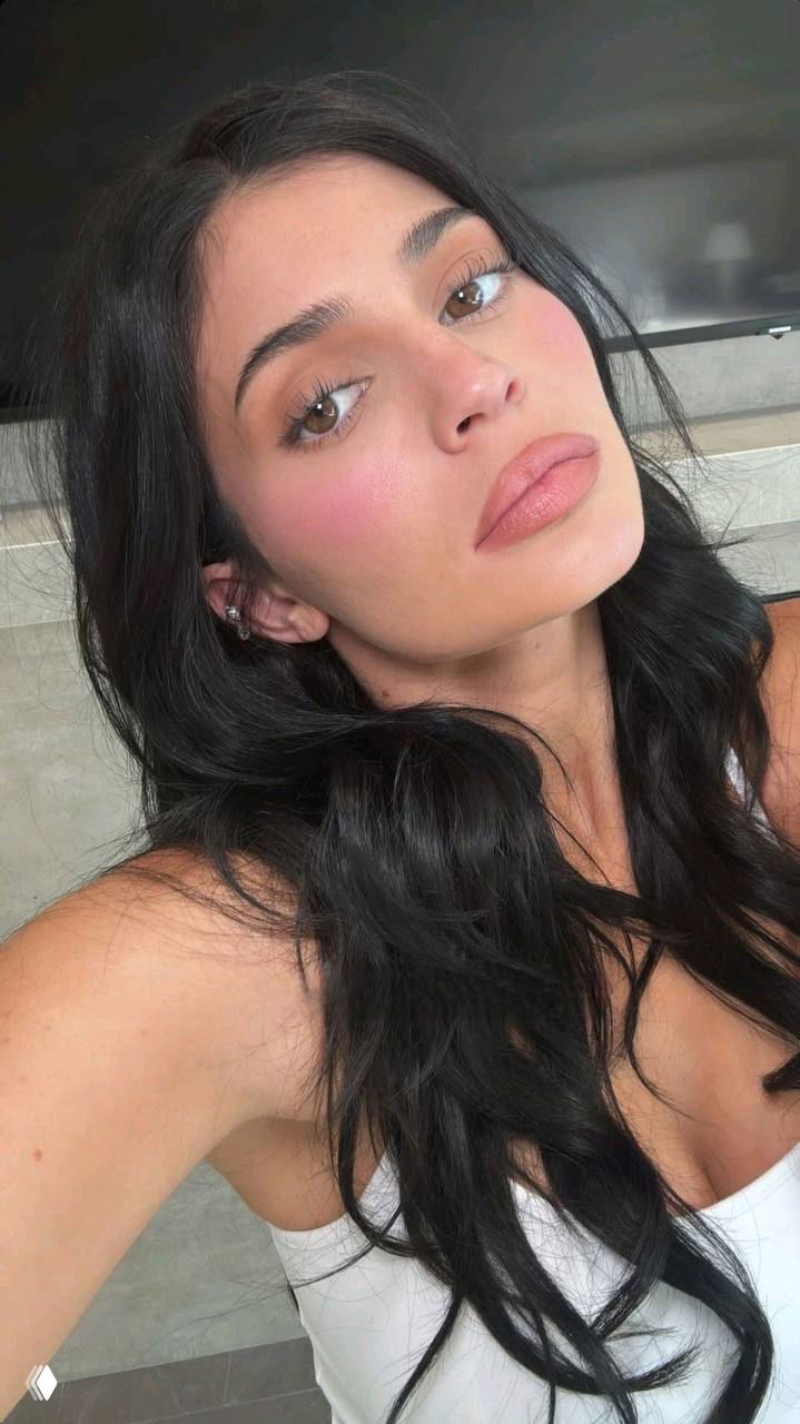 Крупный план лица женщины с естественным макияжем: нейтральные тени, розовые румяна и нюдовые губы с сатиновым финишем, тёмные волосы свободно ниспадают