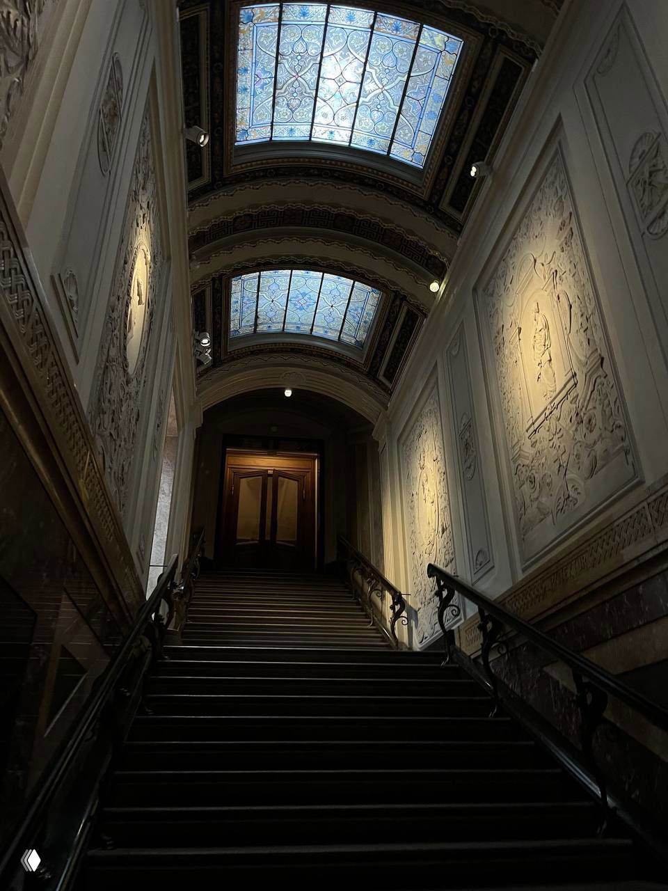 Интерьерная фотография торжественной лестницы в историческом помещении с витражными потолочными окнами, барельефами и приглушённым светом