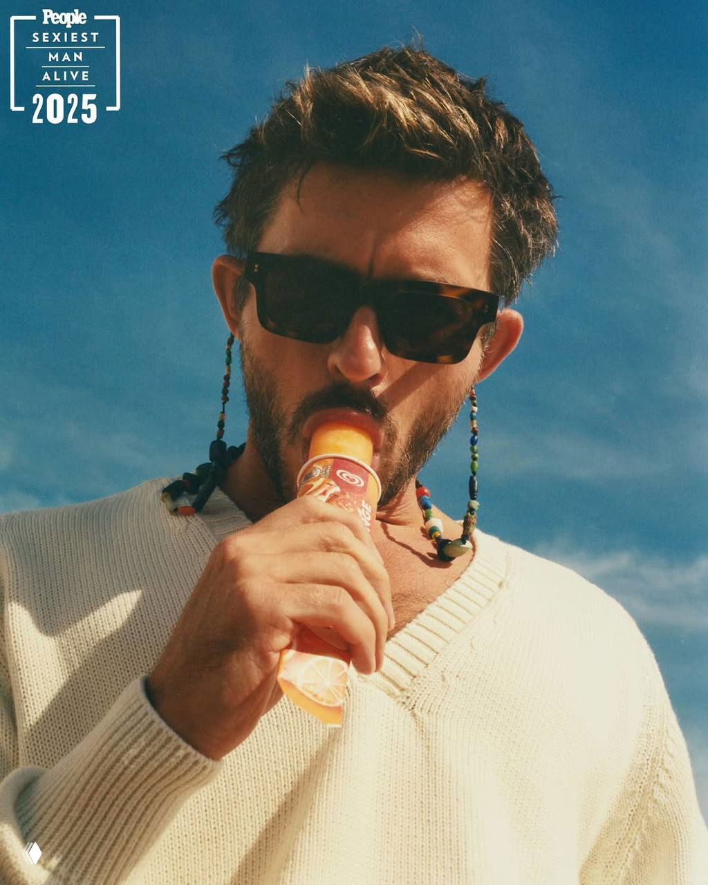 Джонатан Бейли в солнцезащитных очках ест мороженое на фоне голубого неба; кадр подчёркивает летнюю атмосферу фотосессии People 2025.