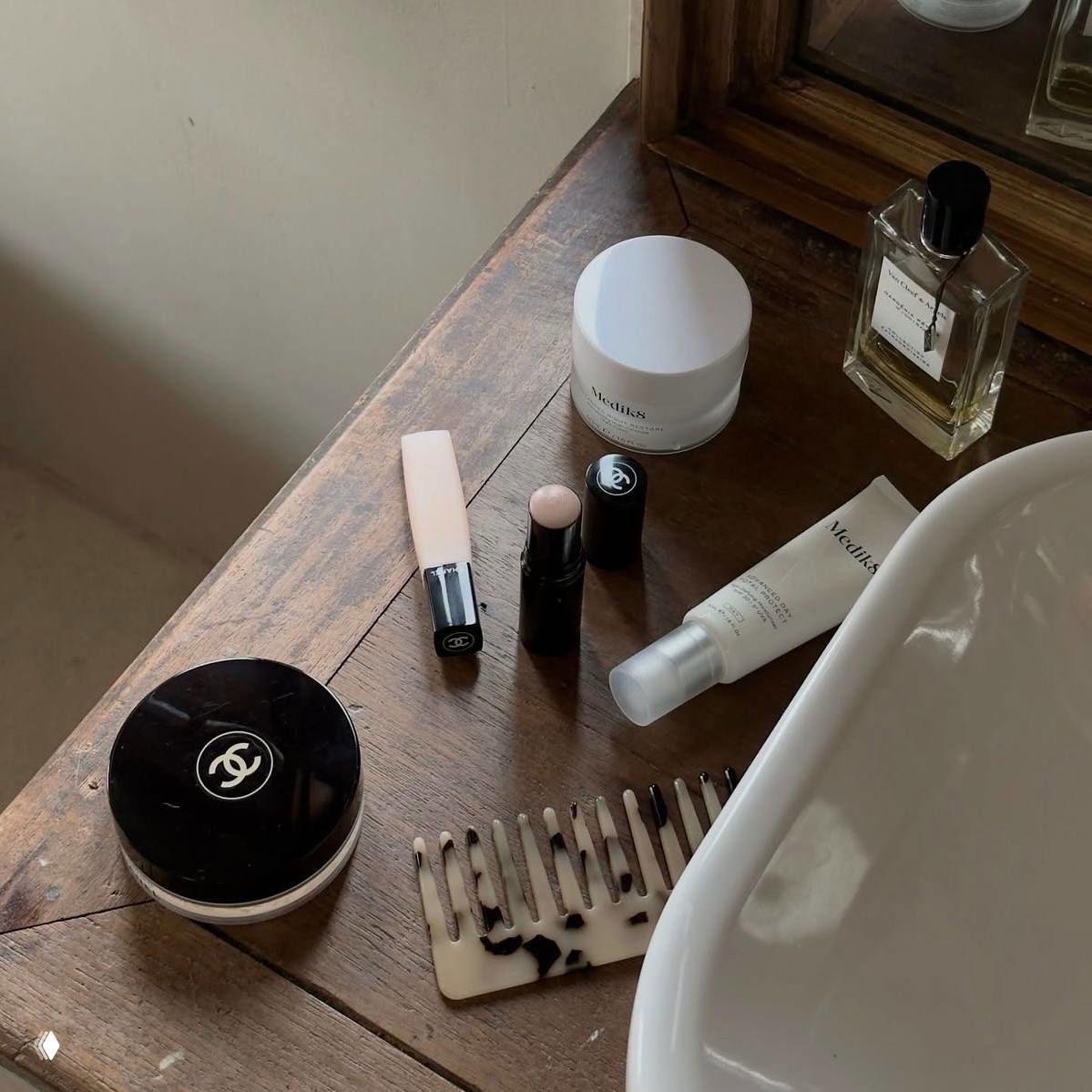 Кадр с косметикой на деревянном столе: баночка крема, помада, тушь и духи — аккуратная композиция средств по уходу и макияжу.