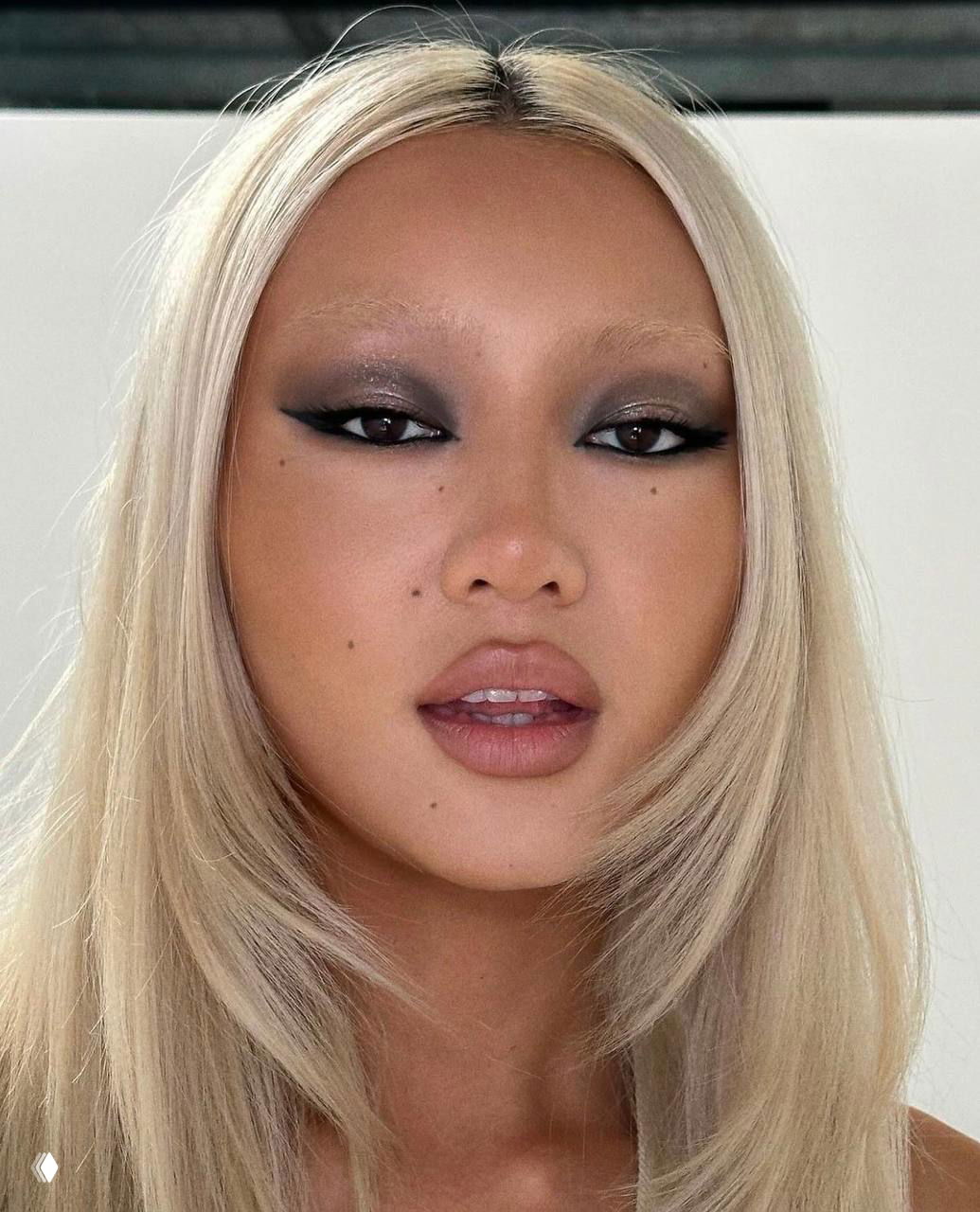 Портрет модели с платиновыми волосами и выразительным чёрным смоки-айз: ровная кожа, нейтральная губная помада и аккуратный контур лица на светлом фоне.