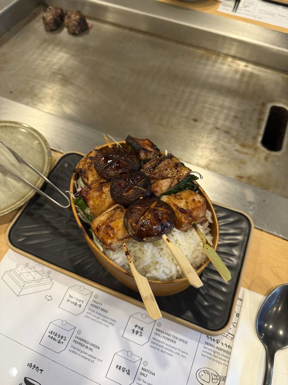 Шпажки с якитори, поданные в миске с рисом на фоне рабочей поверхности гриля — композиция блюда в ресторане.