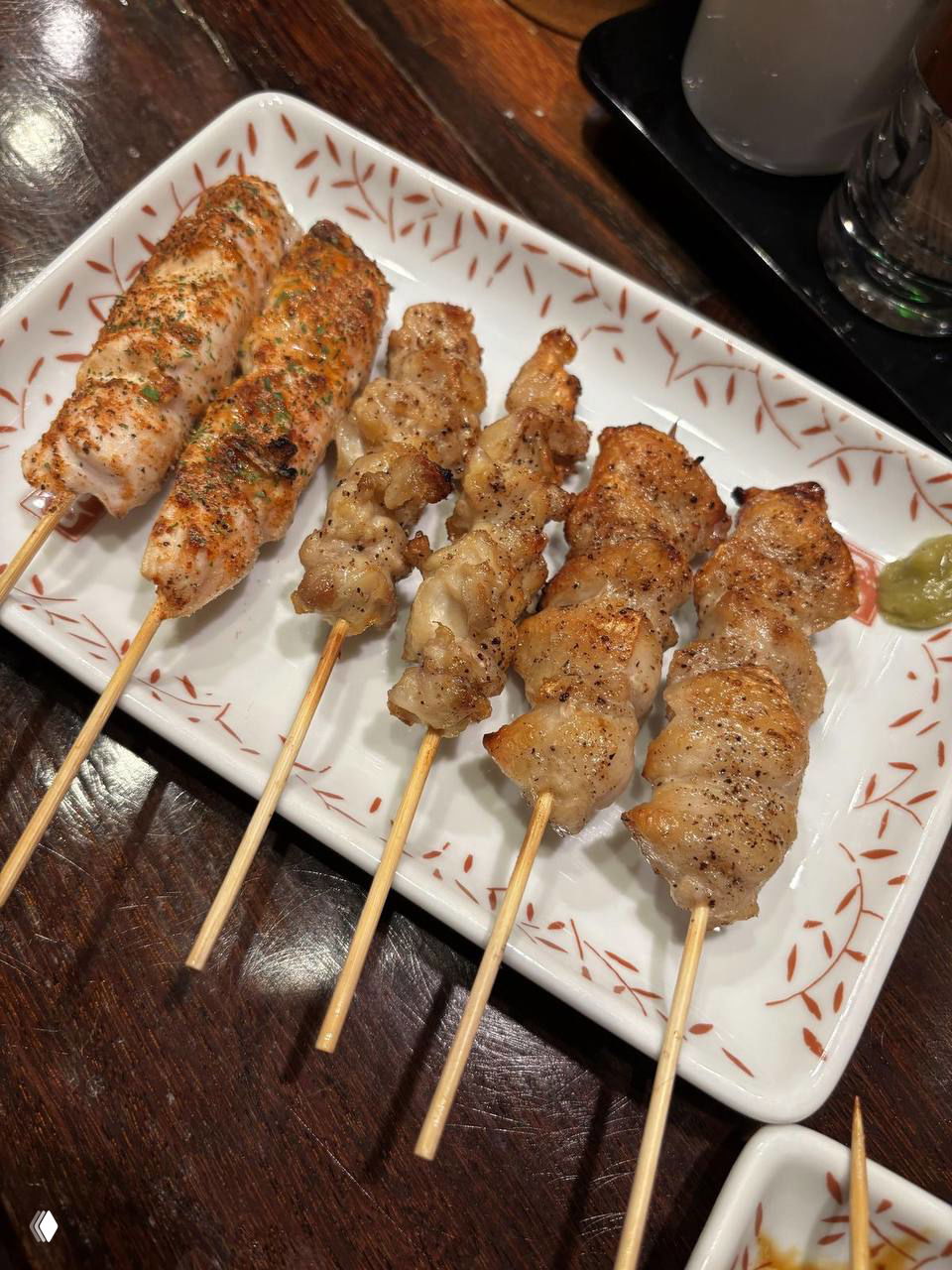 Ряд из нескольких шпажек якитори на белой прямоугольной тарелке: ровные кусочки курицы с лёгкой корочкой и приправами.