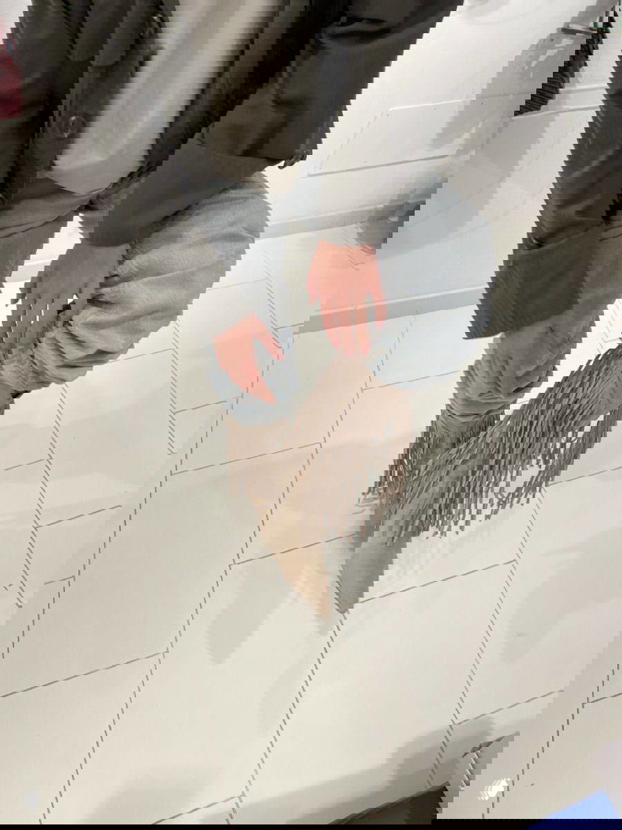 Крупный кадр: человек в светло‑бежевых замшевых сапогах с длинной бахромой, заправленных в свободные джинсы; уличный бохо‑образ на белой плитке.