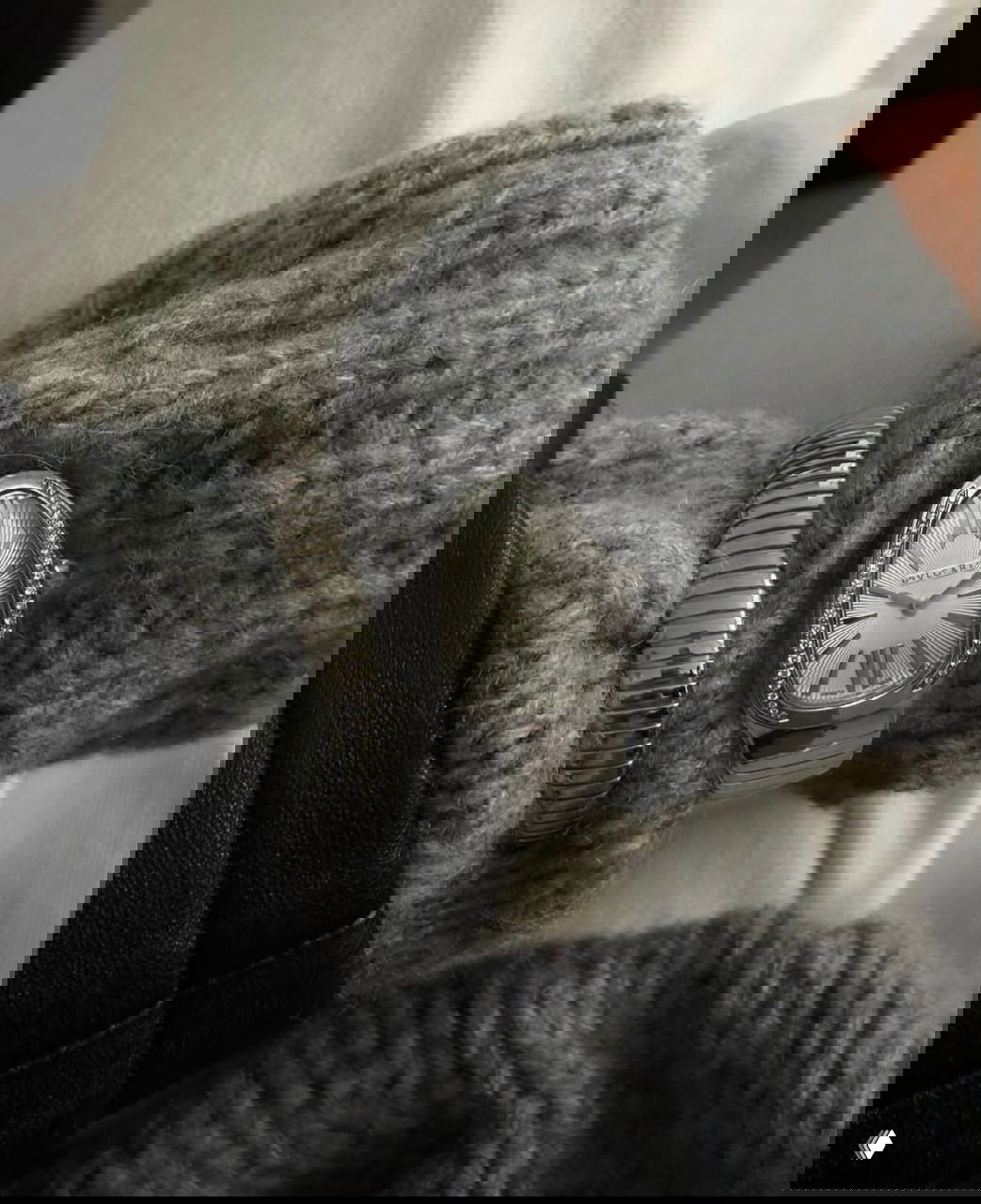 Крупный план запястья в тёплом вязаном свитере с серебристым браслетом и овальными часами на металлическом браслете, нейтральная гамма