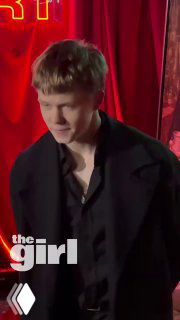 Портрет Тимофея Кочнева на красной дорожке: молодой актёр в тёмном пиджаке на фоне неоновых красных декораций и логотипа theGirl.